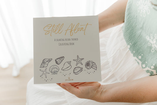 Woman holding a Still Afloat ocean colouring book on her lap, keep one and gift one