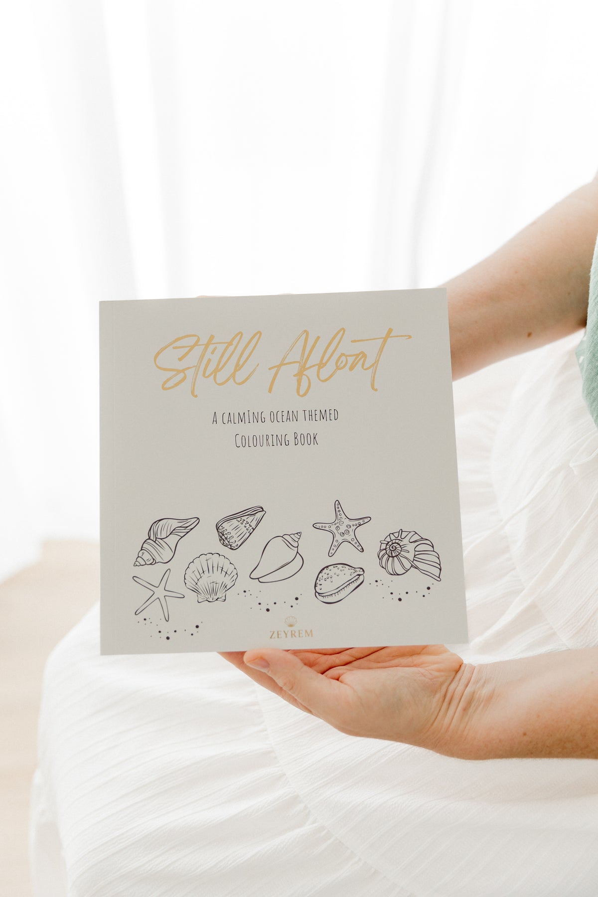 Still Afloat ocean colouring book held on the lap, a calming grief and sympathy gift from Zeyrem Australia