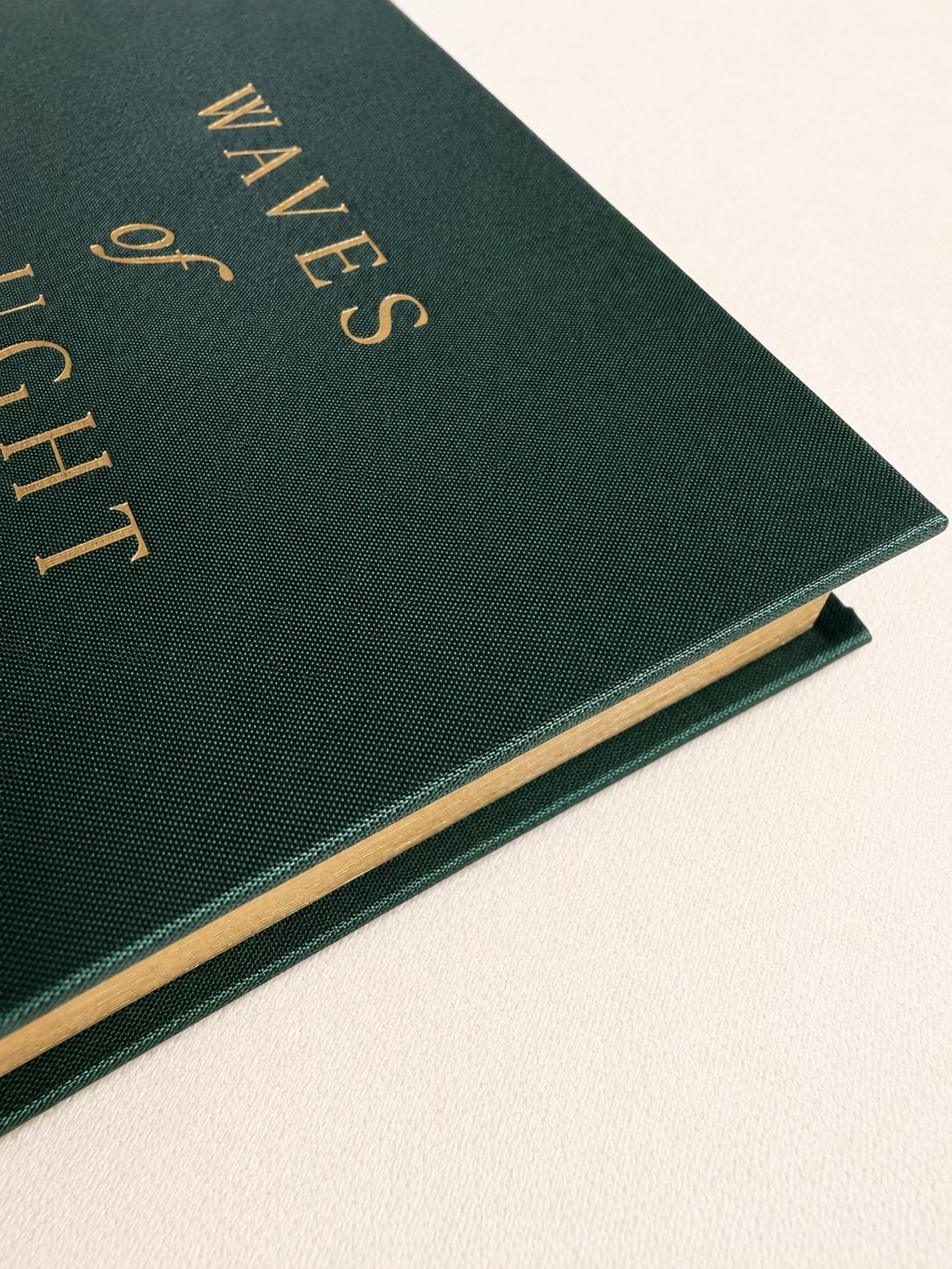 Guided grief journal for loss standing upright, gold foil wave emblem on a forest green linen cover